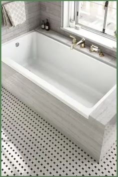 a white bath tub sitting under a window next to a tiled floor and counter top