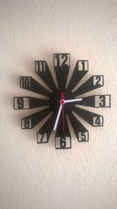 a black clock with red hands and numbers on the face is hanging on a wall