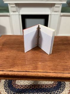 an open notebook sitting on top of a wooden table in front of a fire place