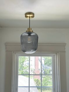 a light fixture hanging from the ceiling in front of a window with white walls and windowsill