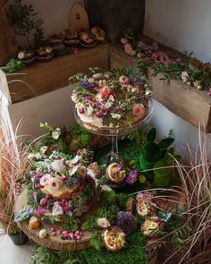 three tiered cake stand with flowers and plants on top, surrounded by greenery