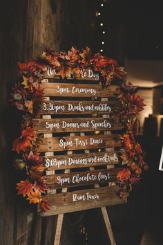 a wooden sign with fall leaves on it in front of a wall that says, autumn is here