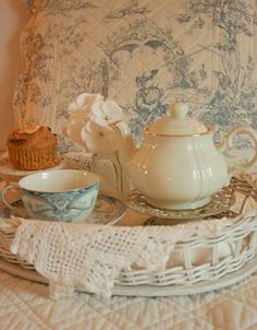 a tea pot and two cups on a wicker tray next to a cupcake