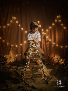 a young boy sitting on top of a ladder surrounded by star shaped lights and stars