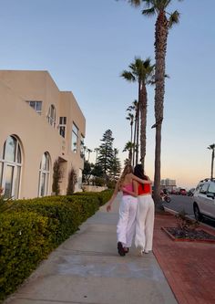 two women walking down a sidewalk next to palm trees