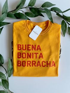 "Buena, Bonita, Borracha Shirt  A play on words from the famous saying \"Bueno, bonito barato\"  T-shirt: Unisex sizing Color Gold 50% Polyester, 50% Cotton Image is sublimation" Spanish Shirts, Play On Words, Katy Tx, Fashion Inspo Outfits, Style Me, Shirt Designs, Fashion Inspo, Tee Shirts, Tshirt Designs