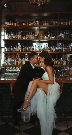 a bride and groom kissing in front of a bar with liquor bottles on the shelves