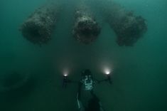 two divers in the water with their lights on and some underwater objects above them,