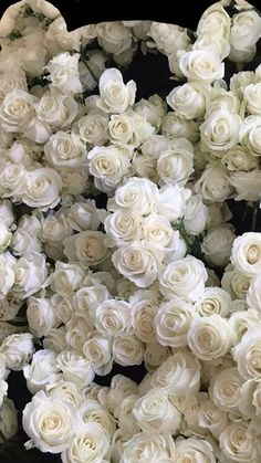 a bunch of white roses are arranged in a circle on a table with black background