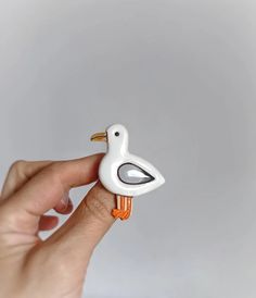 a hand holding a small white and orange bird figurine on it's finger