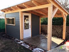 a small gray shed with a white door and wooden frame on the side of it