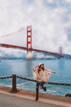 a woman is standing by the water with her arms spread out in front of the golden gate bridge