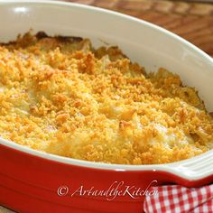 a red casserole dish with cheese and bread crumbs in it on a checkered cloth