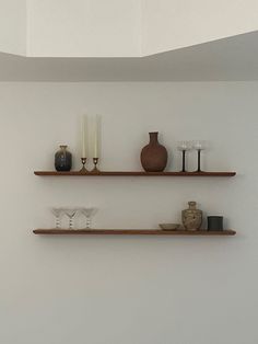 two wooden shelves with vases and candles on them against a white wall in a living room