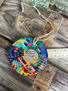 a heart shaped ornament hanging on a piece of wood next to a measuring tape