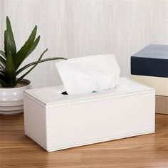 a white tissue box sitting on top of a wooden floor next to a potted plant