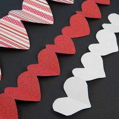 paper hearts are lined up on a black surface with red and white stripes in the background