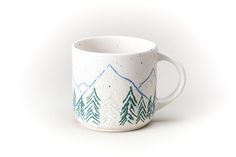 a white coffee cup with trees painted on it