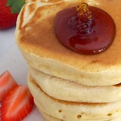 a stack of pancakes with syrup on top and strawberries next to it in the background