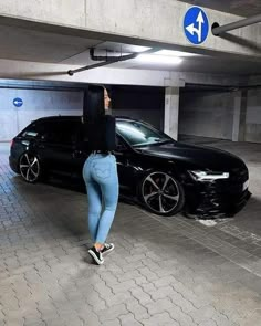 a woman standing next to a black car in a parking garage with an arrow pointing up