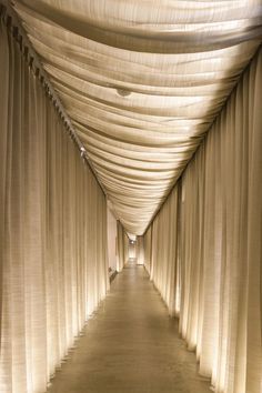 a long hallway with white drapes covering the walls and floor, leading to an entrance