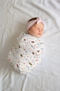 a baby wrapped in a blanket sleeping on top of a white sheet with pink headband