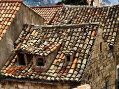 an old stone building with tiled roofs and mountains in the background