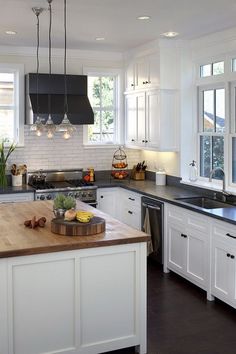 a kitchen with white cabinets and black counter tops, an island in the middle has fruit on it