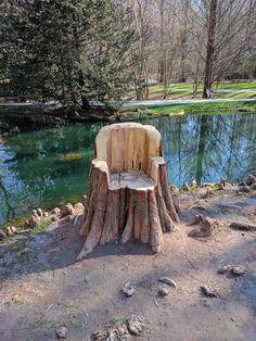 a wooden chair sitting on top of a tree stump next to a lake in the woods