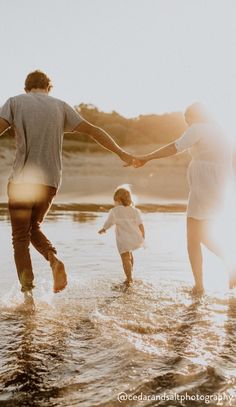 a man and woman holding hands while walking in the water with a child on their lap