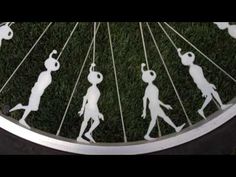 the silhouettes of people walking on grass in front of a bicycle wheel