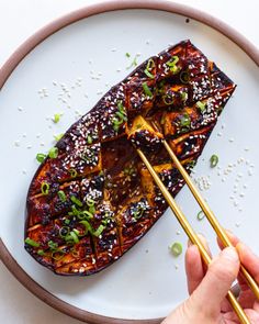 someone holding chopsticks over a plate with food on it