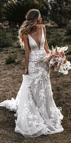 a woman in a wedding dress is walking through the field with her bouquet and flowers