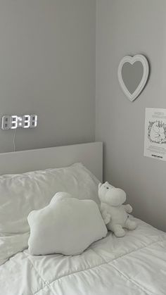 there is a white teddy bear sitting on the bed in this room with grey walls