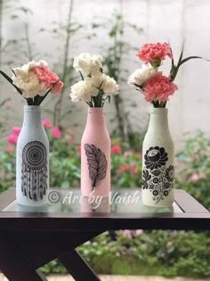 three vases with flowers in them sitting on a wooden table next to some plants