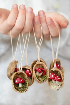 three small mushrooms are hanging from twine with moss and little red mushrooms in them