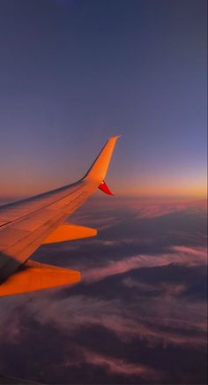 the wing of an airplane as it flies above the clouds at sunset or dawn in the sky