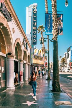 a woman is walking down the sidewalk in front of a movie theater with palm trees