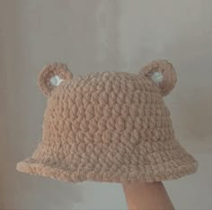 a crocheted bear hat with ears is held up to the side by someone's hand