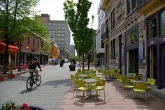 a man riding a bike down a street next to tables with yellow chairs on them