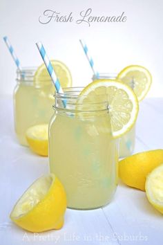 three mason jars filled with lemonade sitting next to sliced lemons and blue striped straws