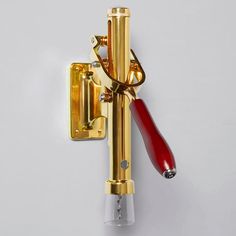 a gold and red wall mounted toothbrush holder on the side of a white wall