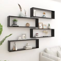 three black shelves on the wall above a white couch in a room with plants and pictures