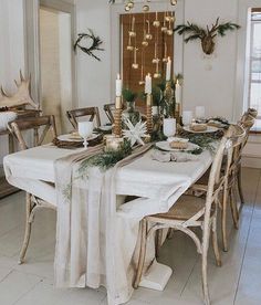 a dining room table set for christmas with candles and greenery on the table runner