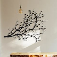 a metal tree branch hanging on the wall next to a wooden bench and light bulb