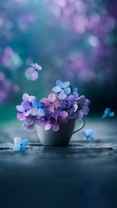 a cup filled with purple and blue flowers on top of a wooden table next to butterflies