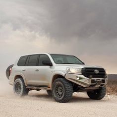 a white truck driving down a dirt road under a cloudy sky with dark clouds in the background