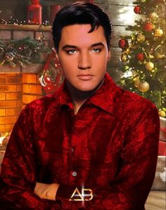 a man in a red shirt standing next to a christmas tree