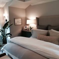 a bed with white sheets and pillows in a bedroom next to a large potted plant