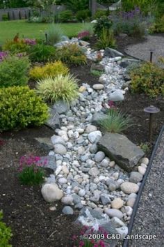 a garden with rocks and flowers in the center, along side a path that leads to a house